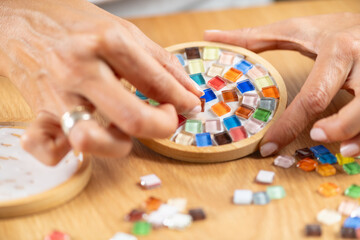 Arranging small craft pieces and gluing them onto coasters in a home studio. Captures precision, texture control, and focused creative workflow.