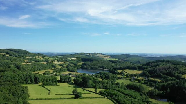 Scenic aerial view of lush green hills, forests, and a tranquil lake in the Morvan region on a clear summer day. Picturesque rural landscape with open fields and scattered trees.