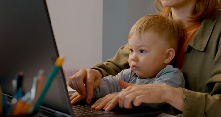 Mother balances remote work and childcare as she types on her laptop with her baby beside her, showcasing the blend of family and work life in a cozy home office.
