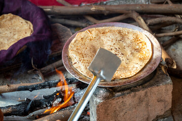 A close-up shot of a traditional Indian chapati being cooked on a clay stove and griddle in a rural village kitchen. This image represents authentic Indian culture, rural happy lifestyle