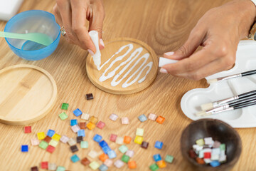 Female hands adding glue while designing decorative coasters. Highlights coordination, slow craft rhythm, and structured artistic technique.
