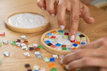 Attaching small elements to coaster surfaces using glue. Emphasizes careful placement, focus, and structured artistic assembly.