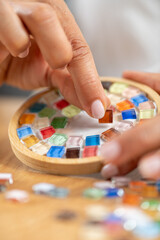 Woman designing coasters by gluing details onto a base. Shows fine-material handling, artistic intent, and controlled craft technique.