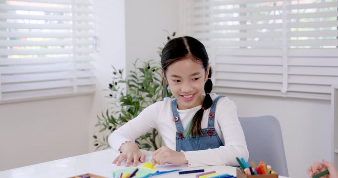 Asian preteen girl smiling happily while working on drawing with colorful stationery, elementary student enjoying art study classroom desk, childhood education creativity practice and learning moment
