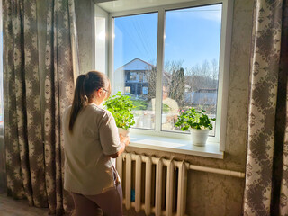 A woman places a pot of geraniums on a sunny windowsill. She tends to her indoor garden and enjoys the bright morning view, a peaceful, domestic moment of care and renewal.