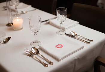 An intimate Valentine's tablescape with crisp linen, silverware, and a tell-tale lipstick mark, evoking luxury romance and sophisticated dining.