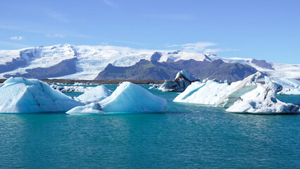 Massive glacier meets a glacial lagoon with floating blue icebergs under a blue sky