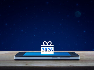 Gift box happy new year 2026 flat icon on modern smart mobile phone screen on wooden table over fantasy night sky and moon, Business happy new year 2026 shop online concept