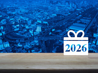 Gift box happy new year 2026 flat icon on wooden table over modern city tower, street, expressway and skyscraper, Business 2026 shop online concept