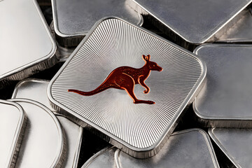 A close-up of several square silver bullion bars. The central bar features a detailed, copper-colored kangaroo silhouette set against a textured, sunburst radial background.