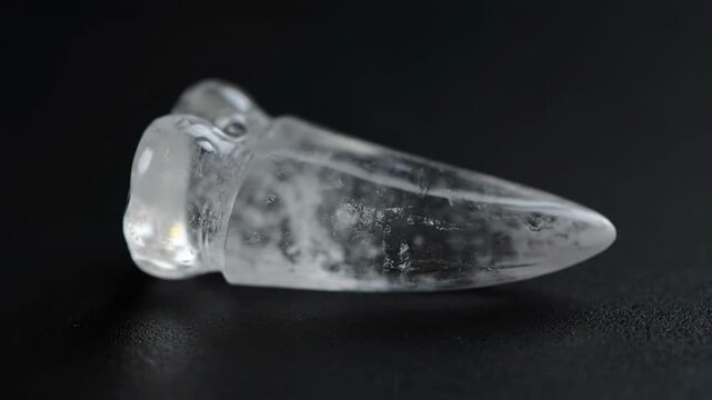Close up of clear quartz crystal carved in shape of a tooth on dark background
