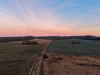 Obraz premium wide rural landscape with open fields, a dirt path, and soft pastel skies during sunset, evoking a calm and peaceful countryside evening