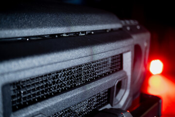 Detailed view of rugged vehicle grille with protective mesh and matte surface illuminated by red...