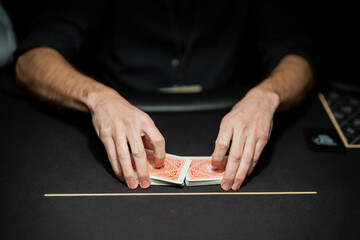 Professional poker dealer hands arranging playing cards on casino table felt, focused on procedural card control within live gambling environment