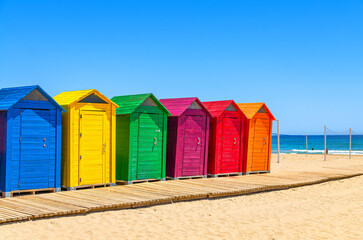 Playa de San Juan beach in Alicante city, wooden colorful storage huts sheds cabins for sports equipment and wooden boardwalk paths on sandy beach in sunny summer day, Valencian Community, Spain