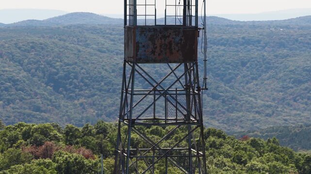 Aerial telephoto orbit of fire lookout tower rising above forest with birds soaring in backdrop, Devils Knob in Arkansas, medium