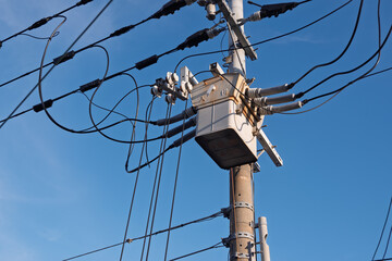 青空にそびえる電柱最上部の高圧柱上開閉器と配線、電力供給インフラの風景