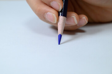 Close up of a hand drawing with a blue colored pencil on white paper