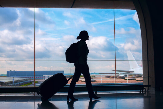 airport, silhouette of woman passenger walking with luggage to take flight in modern airport