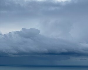 Dramatic cloudy sky over calm sea horizon. Minimal atmospheric seascape with layered storm clouds, soft light and suitable for weather, climate, background.