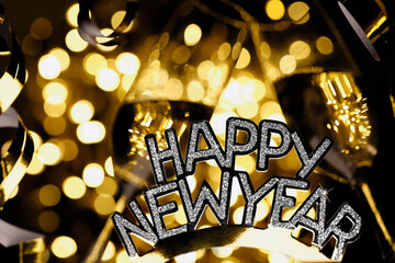Happy New Year lettering in front of champagne glasses, fireworks, streamers and golden bokeh lights, festive background for New Year's celebrations