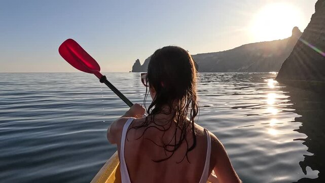 Kayaking woman sea paddling calm water near cliffs at sunset, peaceful adventure