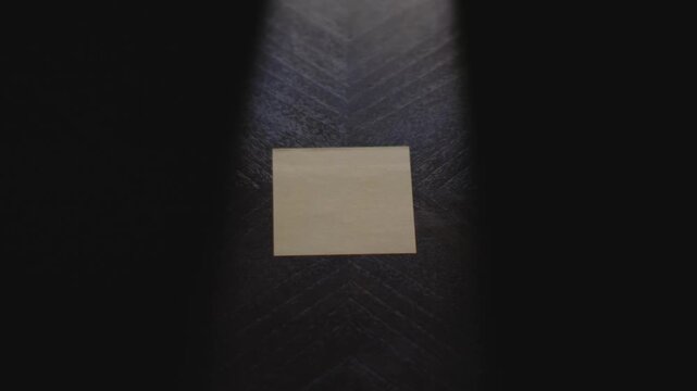 A dramatically lit close up of a hand placing down a Post it note and drawing the number 8 in marker.