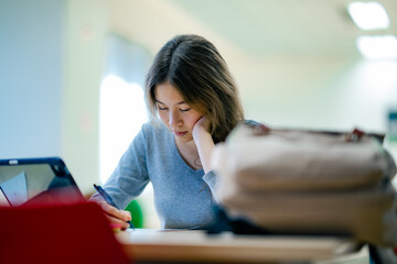 Female student studying with tablet computer at library table surrounded by textbooks representing online learning, education technology, focused study time