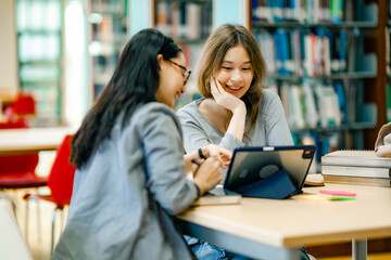 Female students learning through tablet at library with books representing blended learning digital education