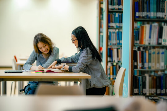 School homework support scene with student reading textbook at library table guided learning atmosphere. Private tutor guiding student at library table, personalized learning education support.