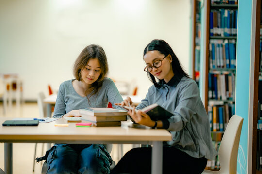 One on one tutoring session with tutor explaining lesson from textbook at library focused mentoring. Private education support scene with tutor student reading book together at library desk.