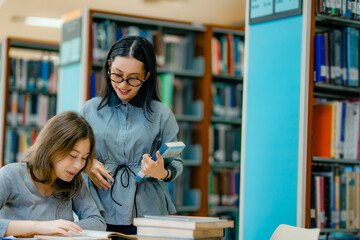 Tutor teaching student through reading books at library table explaining academic content...