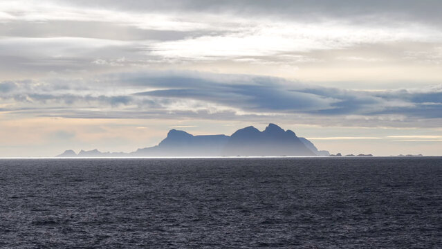 Silhouette of a distant mountain island across a dark, vast ocean