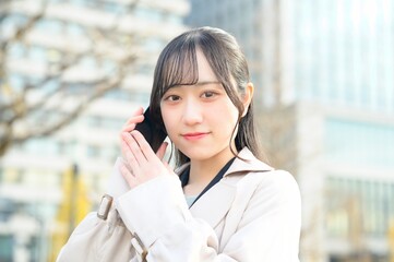 オフィス街でスマホを使用する20代のビジネスウーマン