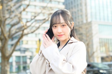 オフィス街でスマホを使用する20代のビジネスウーマン