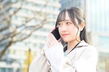 オフィス街でスマホを使用する20代のビジネスウーマン