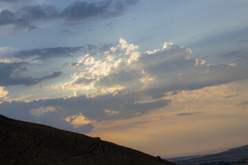 Dramatic sky with sun rays breaking through clouds over a silhouette of a hill