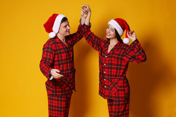 Fototapeta premium Happy couple in Santa hats and pajamas on orange background, space for text. Christmas atmosphere