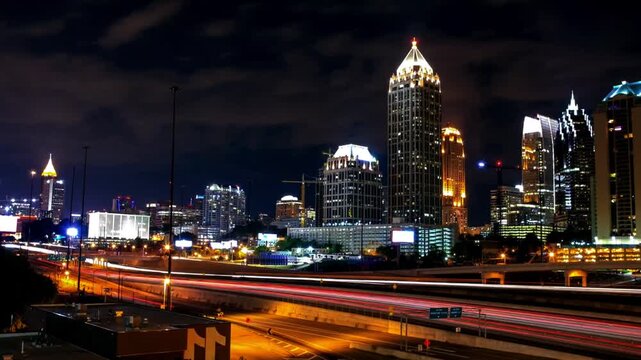 Bustling urban night scene featuring a modern city skyline, illuminated skyscrapers, and fast-moving traffic along a highway. Long-exposure light trails create energy and drama in the metropolitan lan