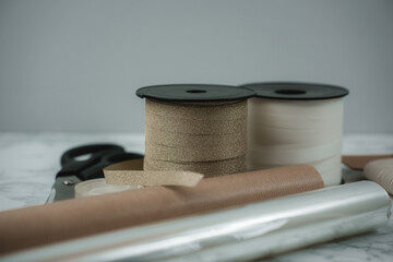 All materials for wrapping gifts during the festive season are organized on a smooth surface. Ribbons, scissors, and rolls of paper await the hands ready to create beautiful presents.