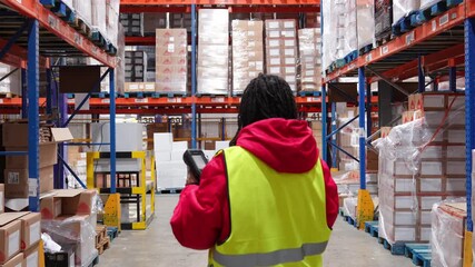Young female logistics employee using a barcode scanner for inventory management while walking down a large, cold storage warehouse aisle - Powered by Adobe