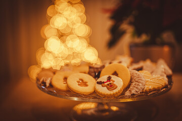 Christmas cookies close up. Christmas cookies on a glass tray. In background Christmas tree. Christmas lights.