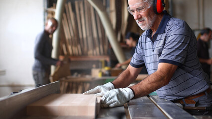 Senior carpenter cutting wood plank using industrial saw