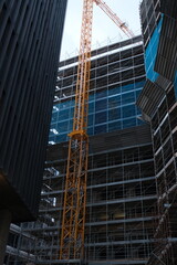 Fototapeta premium Urban construction site with scaffolding and yellow tower crane between modern buildings