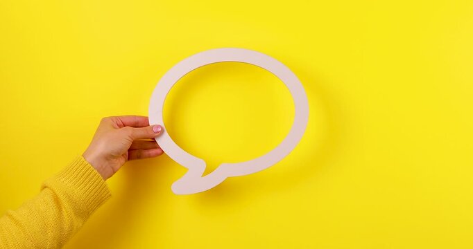4K footage of a hand holding a speech or dialogue bubble symbol against a yellow background, representing communication, conversation, chat, or messaging concepts.