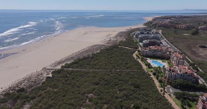 Aerial drone shot of coastal resort complexes and hotel developments beside wide sandy beach and Atlantic Ocean at Isla Canela, Huelva, Andalusia, Spain, showing mass tourism and holiday destination