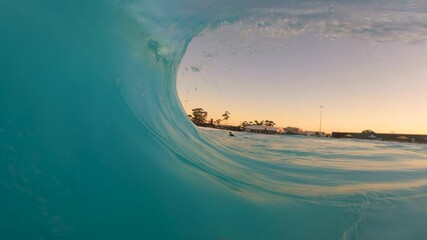 Slow motion point of view showing bodyboarder riding inside crystal clear barrel tube at wave pool leisure centre with early morning dawn sunrise in Australia extreme sports surfing action and fitness