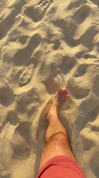 Top shot view POV ugc style video of person walking on sandy beach towards sea. Vacation time holiday season. Man wearing swimsuit pants stepping on sand going for a swim during hot summer day