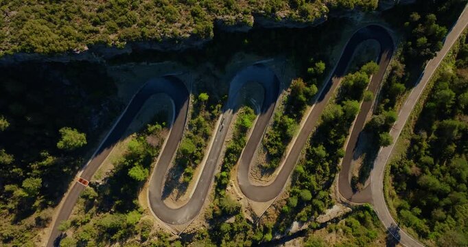 Wide overhead drone static shot reveals cyclists threading steep hairpin switchbacks across a forested mountain overlooking Cinca River gorge in Sobrarbe, with multiple curves visible