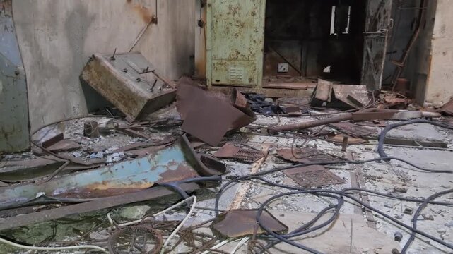 Haunting aftermath of industrial abandonment. Piles of rusted metal, twisted wires, and broken machinery litter the concrete floor of a decaying facility.